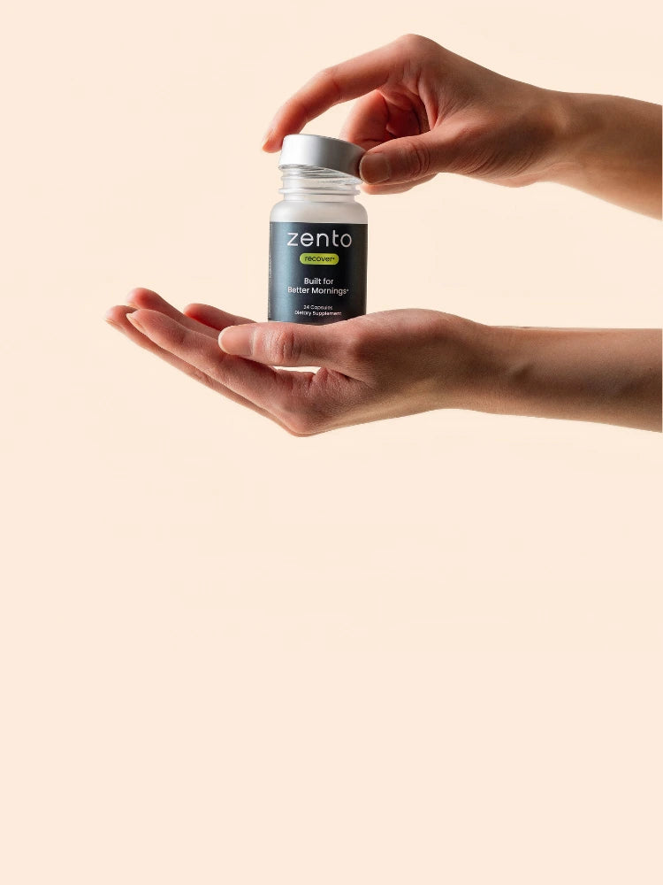 Hand holding a Zento supplement bottle against a beige background